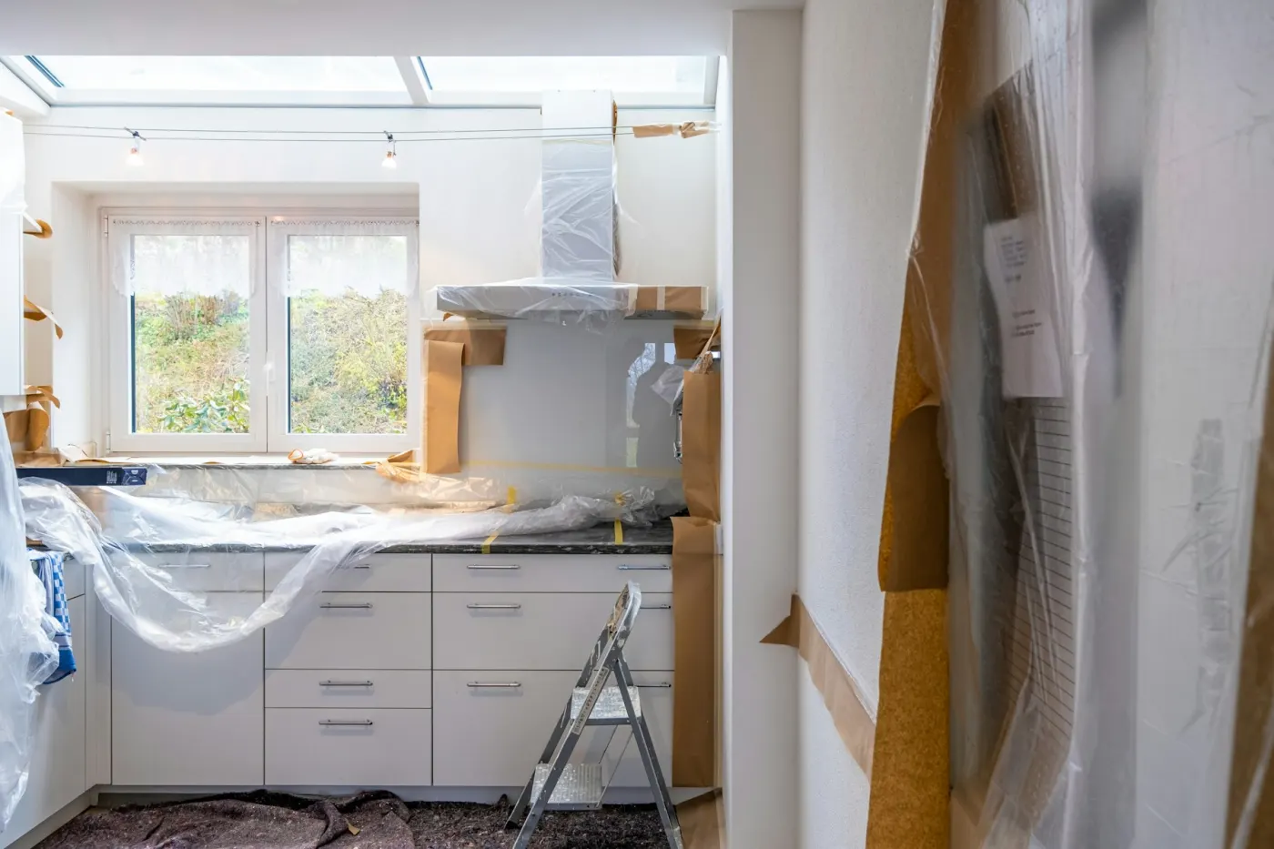 Kök under renovering med vita skåp övertäckta av skyddsplast